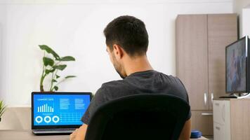 Businessman at home in casual clothes looking on computer screen with animated data chart analysis. Back view. Dolly slider 4K footage video