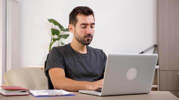 Man typing on the notebook in his living room. He is relaxed and wears casual clothes. Dolly slider 4K footage with parallax effect video