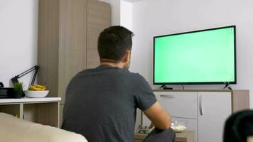 Mann Aufpassen ein groß Grün Attrappe, Lehrmodell, Simulation Bildschirm Fernseher im das Leben Zimmer. 4k Aufnahmen video