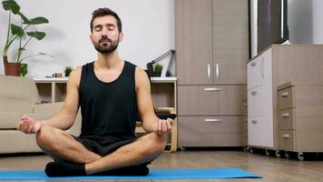 homem às casa praticando ioga dentro a vivo sala. ele sitts dentro a lótus pose medita. boneca controle deslizante 4k cenas video