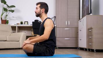 Side view of fit young man stretching on a blue mat on the floor of his flat. He preprares for yoga and is relaxed. Dolly slider 4K footage video