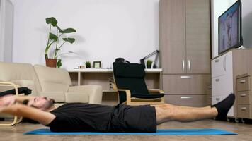 Young fit man exercising at home he is doing crunches on the floor on a blue mat in the living room video