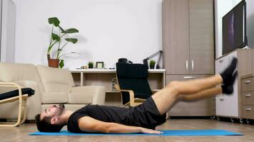 athlétique Jeune homme Faire des exercices pour le abdos sur le sol sur une bleu tapis dans le sien vivant chambre. chariot glissière 4k métrage video