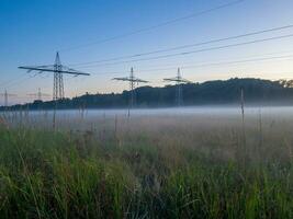 Panoramic image of a meadow with high-voltage pylons and ground fog in autumn photo