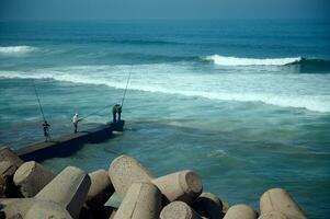 Rear view of unrecognizable people - fisherman standing on the seashore on breakwater and fishing in Atlantic Ocean photo