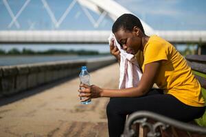 Exhausted woman after exercise drinking water and wiping sweat with towel photo