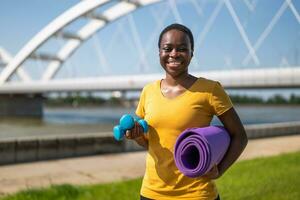 Happy sporty woman holding weights and exercise mat photo