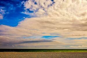 a beach with a cloudy sky and a green field photo