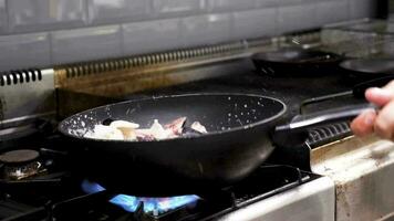 Cook frying seafood and shrimps in a pan on stove in restaurant kitchen video