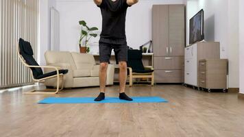 ung atletisk man håller på med knäböj i de levande rum. sport på Hem. panorering upp video