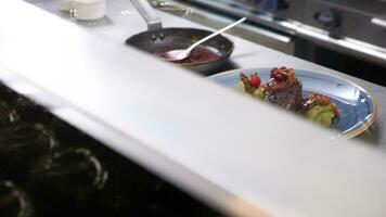 Revealing shot of cook in restaurant kitchen seasoning a plate with grilled beef stake. Close up footage video