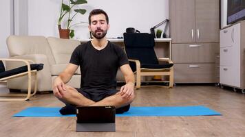 Man meditating in lotus yoga pose and looking at a digital PC in front of him video