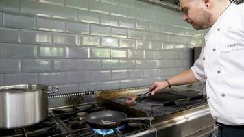 Cook placing a piece of grilled beef meat from the grill to a pan on a stove in restaurant kitchen video