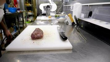 Cook seasoning and preparing a piece of beef meat for grilling in restaurant kitchen video