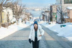 Woman tourist Visiting in Hakodate, Traveler in Sweater sightseeing Hachiman Zaka Slope with Snow in winter. landmark and popular for attractions in Hokkaido, Japan. Travel and Vacation concept photo