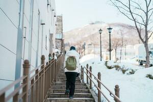 mujer turista visitando en hakodate, viajero en suéter Turismo hachiman zaka Pendiente con nieve en invierno. punto de referencia y popular para atracciones en Hokkaidō, Japón. viaje y vacaciones concepto foto