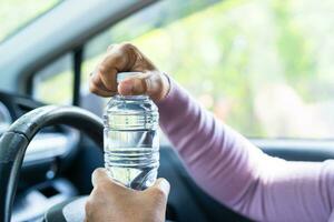 Asian woman driver holding bottle for drink water while driving a car. Plastic hot water bottle cause fire. photo