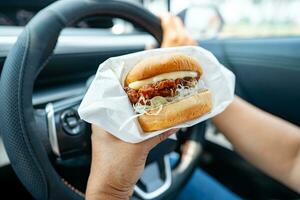 asiático dama participación hamburguesa a comer en auto, peligroso y riesgo un accidente. foto