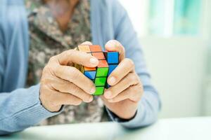 bangkok, Tailandia julio 11 2023 Alzheimer enfermedad anuncio, asiático mayor mujer paciente jugando rubik cubo juego a práctica cerebro formación para demencia prevención. foto