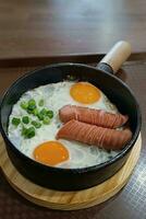 Scrambled eggs in a frying pan with fried meat sausages photo