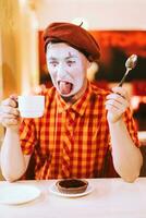 The clown is eating a cake in a cafe and his face is croaking. photo