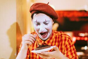 The clown is eating a cake in a cafe and his face is croaking. photo