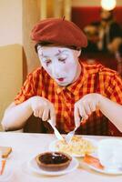 The clown is eating a cake in a cafe and his face is croaking. photo