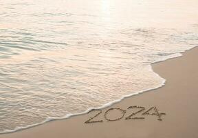 2024 año escrito en el playa en el puesta de sol tiempo. nuevo año 2024 concepto foto