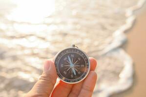 Close up hand holding compass with beach background photo