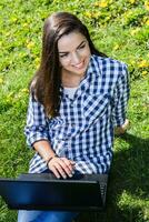 hermosa niña sentado en el parque con un ordenador portátil foto