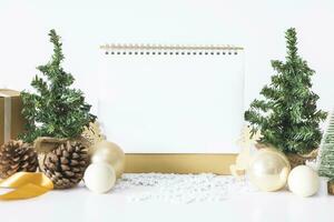 The White calendar mock up to enter text by the festive scene of beautiful Christmas tree adorned, with Christmas balls, pine cones, red house gift box tied golden ribbon. concept about Important day. photo