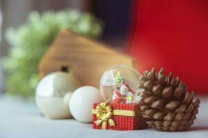 Navidad pelotas, Papa Noel claus en un nieve globo, y pino conos en un color crema paño, conjunto en contra un rojo antecedentes y Exquisito Bokeh. nuevo año celebracion atmósfera, acerca de de importante día. foto