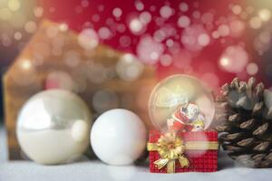 Navidad pelotas, Papa Noel claus en un nieve globo, y pino conos en un color crema paño, conjunto en contra un rojo antecedentes y Exquisito Bokeh. nuevo año celebracion atmósfera, acerca de de importante día. foto