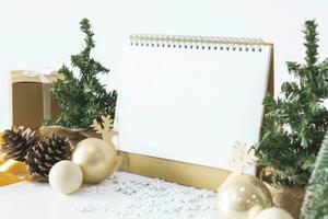 The White calendar mock up to enter text by the festive scene of beautiful Christmas tree adorned, with Christmas balls, pine cones, red house gift box tied golden ribbon. concept about Important day. photo