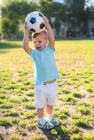 pequeño chico jugando con un fútbol pelota en el campo en verano foto
