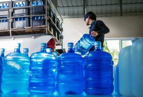 trabajadores levantar Bebiendo agua claro y limpiar en azul el plastico galón dentro el espalda de un transporte camión purificado Bebiendo agua dentro el producción línea pequeño negocio foto