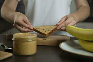 Woman preparing breakfast. Bread with peanut butter and banana. photo