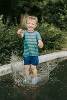 pequeño chico saltando en un charco en verano foto