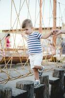 un pequeño chico camina a lo largo un estirado de madera puente en un cuerda pueblo foto