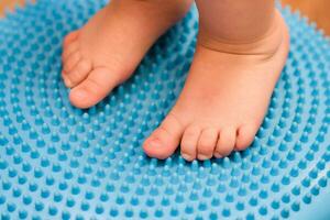 little kid massages his feet while standing on the rug photo