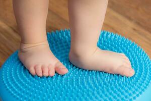 little kid massages his feet while standing on the rug photo