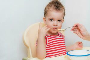 Mom feeds the baby buckwheat porridge in the kitchen photo