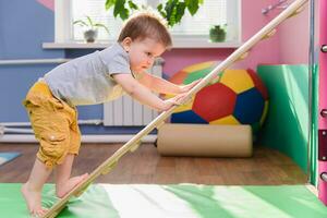 the little boy climbs up a wooden plate in the gym photo