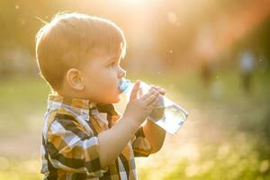 hermoso chico bebidas claro agua desde un botella en un soleado día fuera de foto