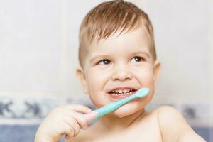 encantador bebé cepillado su dientes con un cepillo de dientes en el baño foto