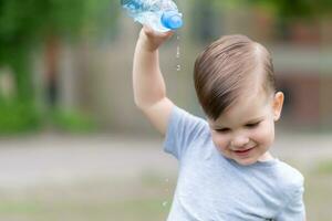 alegre niño vierte agua desde un botella en él mismo foto