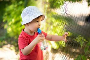 handsome boy drinks clear water from a bottle on a sunny day outside photo