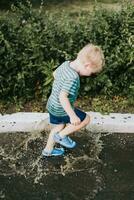 pequeño chico saltando en un charco en verano foto