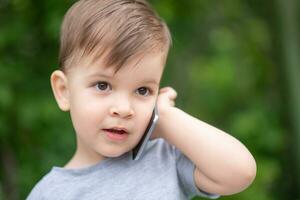pequeño chico habla en el teléfono inteligente en el parque foto