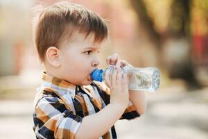 hermoso chico bebidas claro agua desde un botella en un soleado día fuera de foto